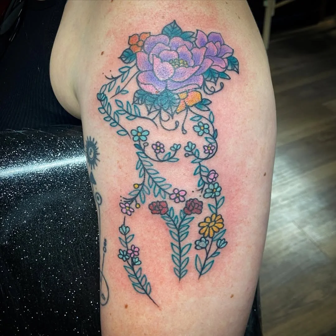 Tattoo of a woman's face outline made of flowers and vines, with a large purple flower at the top.