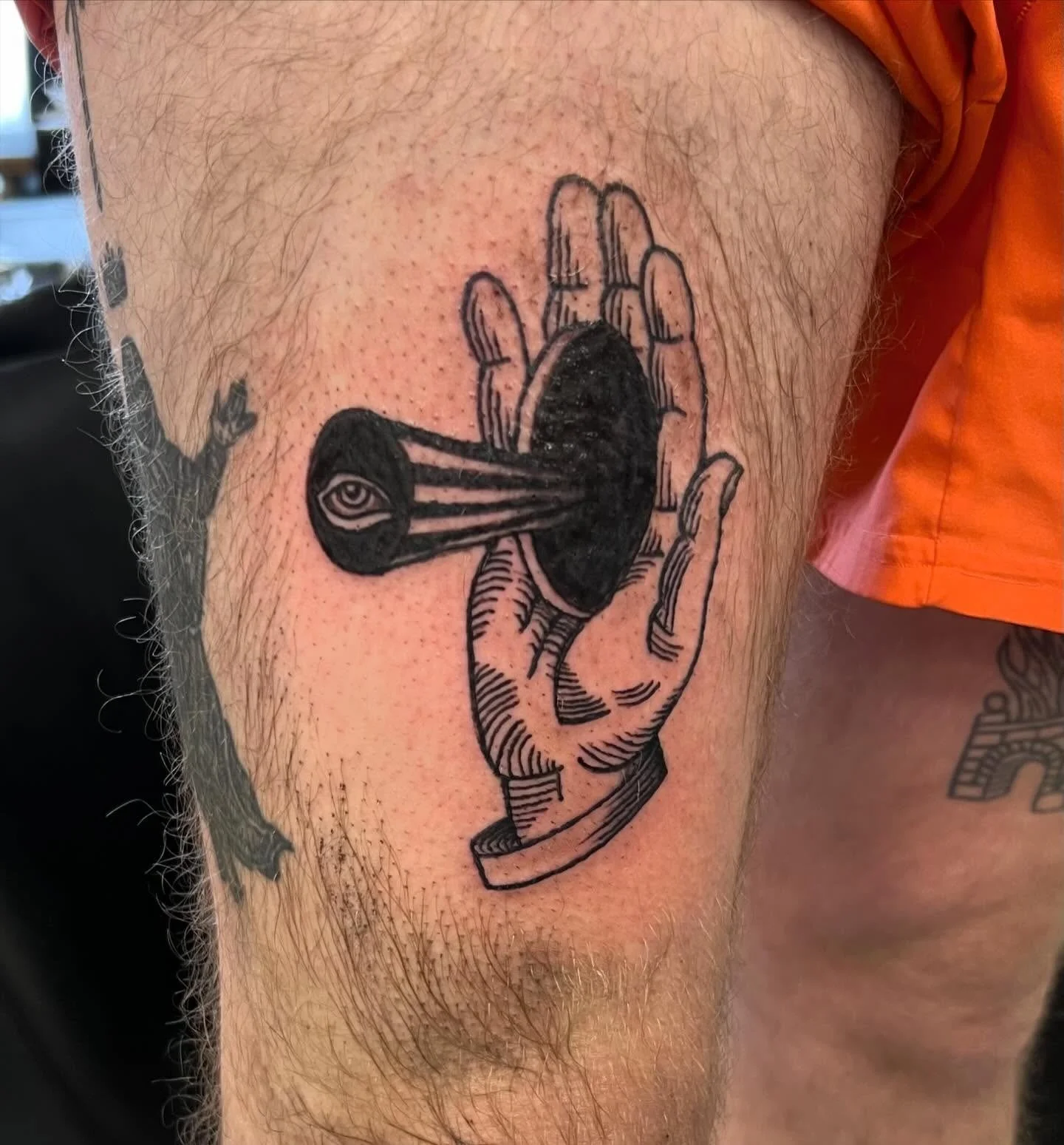 Tattoo of a hand holding an eyeball with a dark circle and lines extending from the eyeball to the hand, on the person's upper thigh.