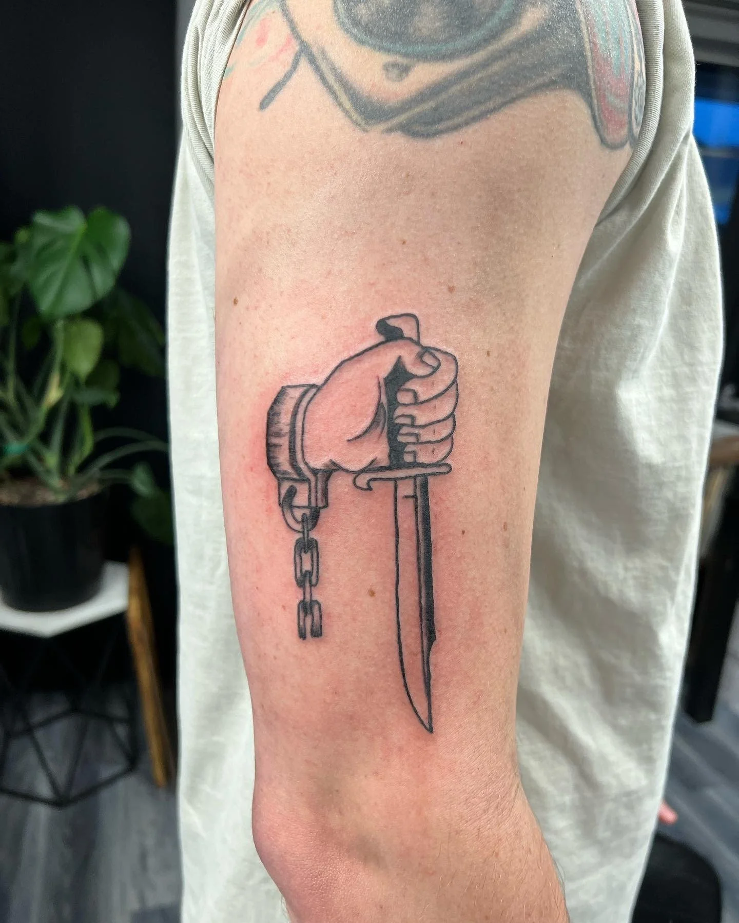 A tattoo on a person's upper arm of a hand holding a dagger with a chain attached to the wrist.