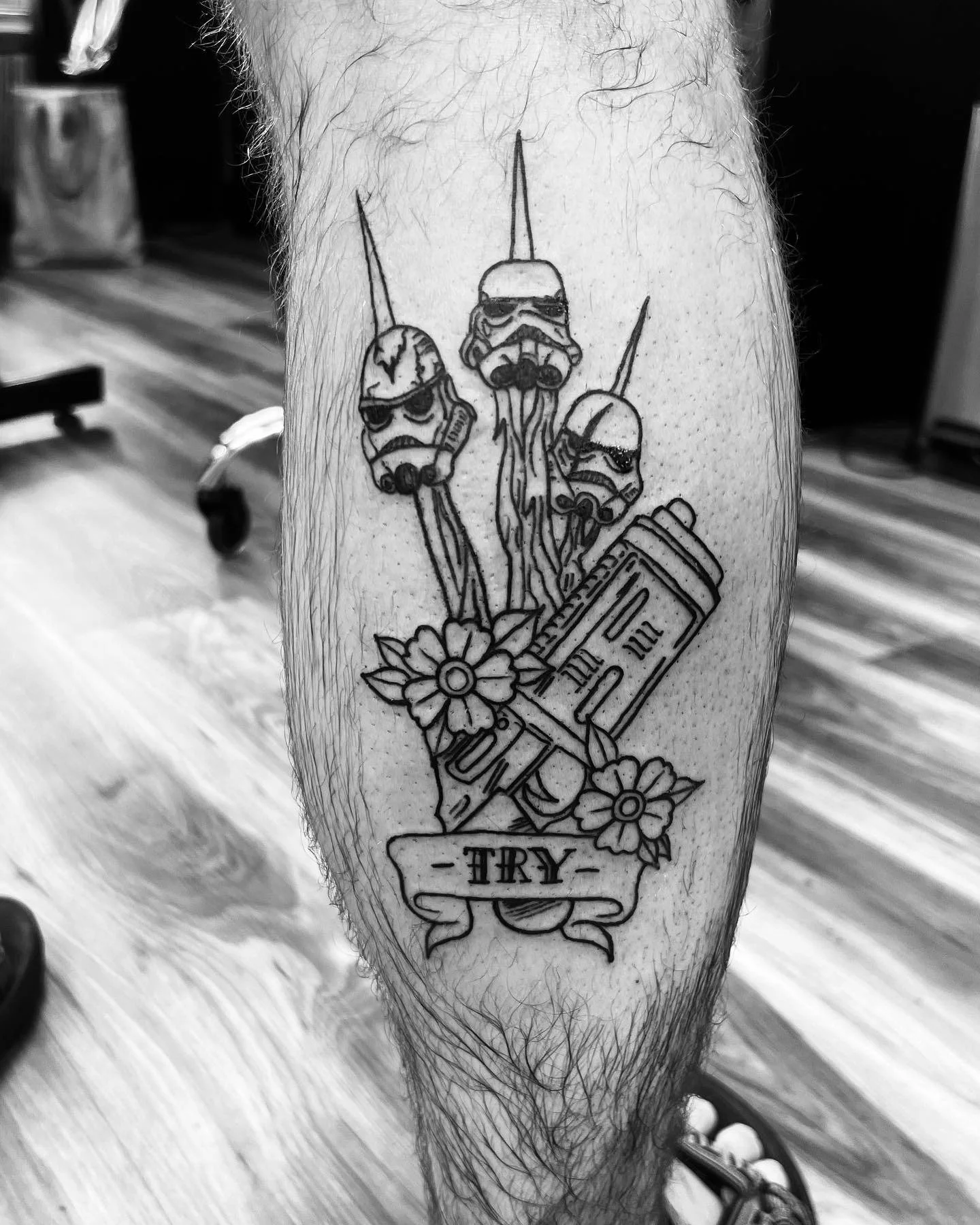 A tattoo of three stormtrooper helmets with crossed blasters, flowers, and a banner with the word 'TRY'.
