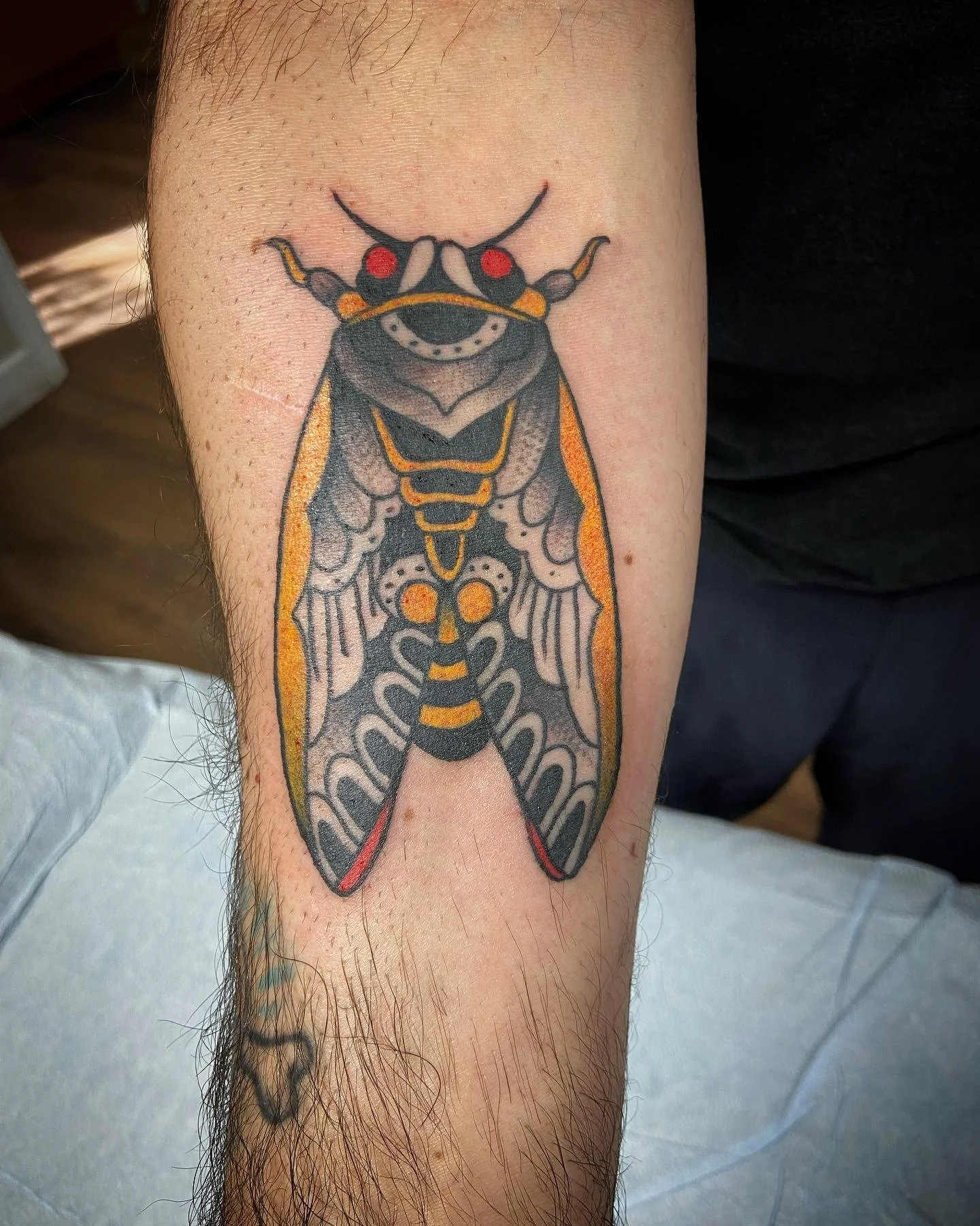 Tattoo of a moth with black, yellow, gray, red, and orange coloring, with detailed wings and antennae.