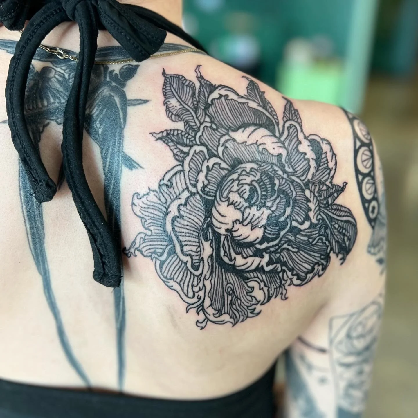 Close-up of a detailed black and gray floral tattoo on a person's shoulder and upper arm, featuring a large, intricate flower with leaves.
