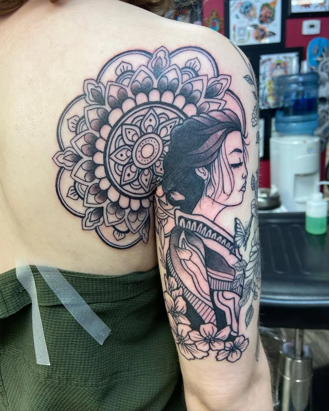 Tattoo on a person's shoulder and upper arm depicting a woman with closed eyes and flowing hair, surrounded by a large mandala and cherry blossoms.