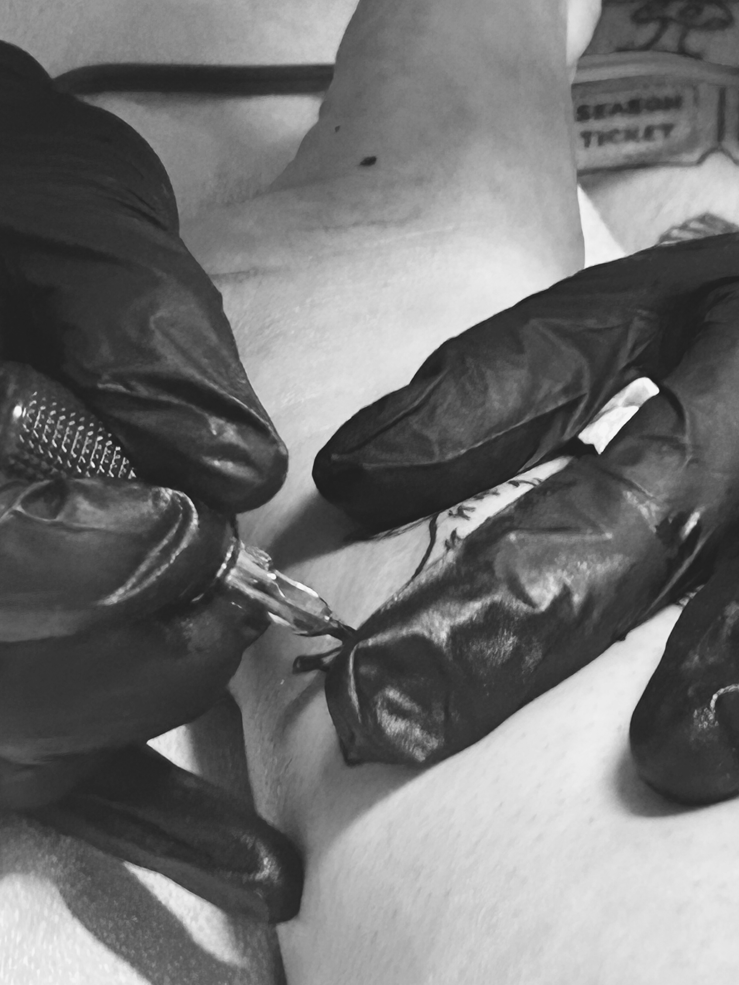 A person wearing black gloves holding a needle, seemingly administering an injection to another person.