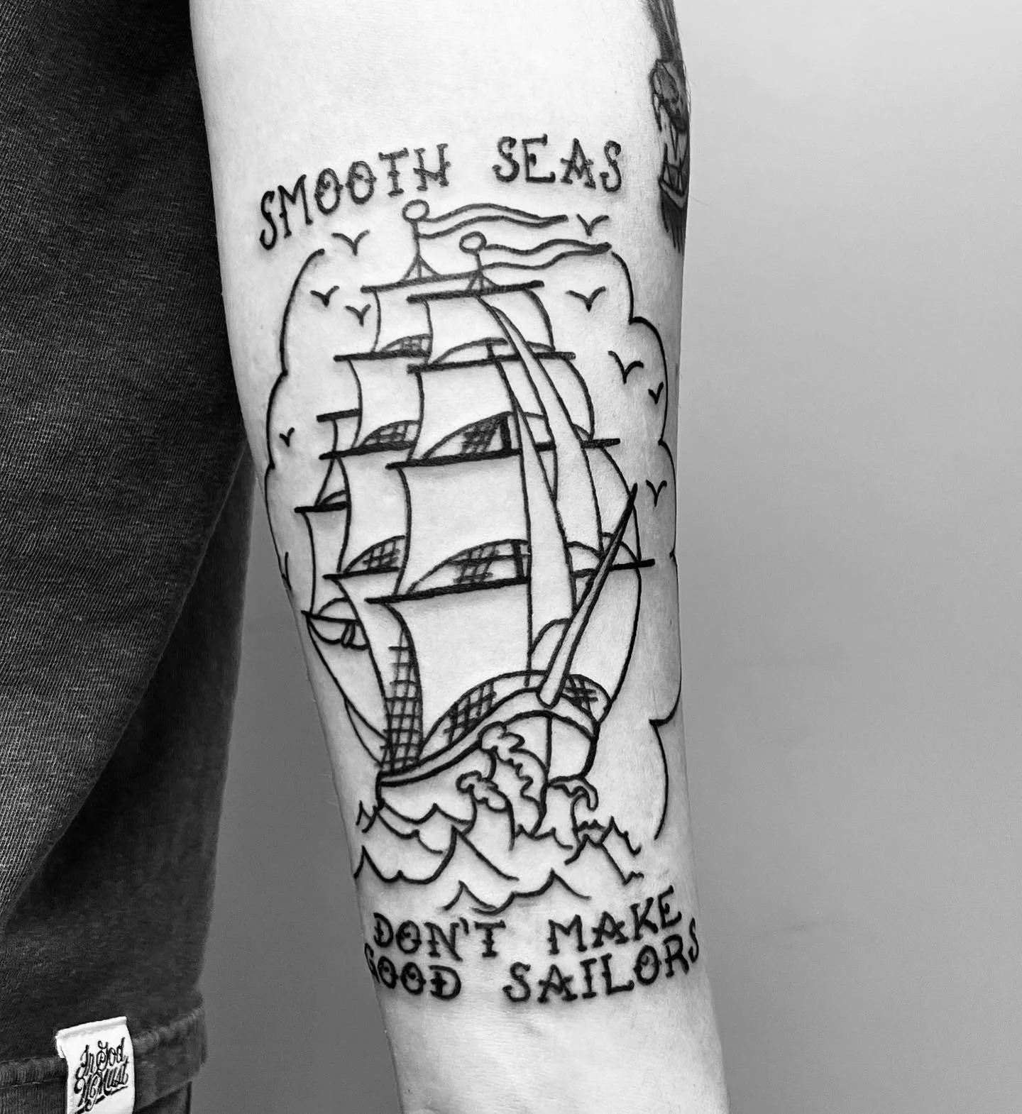 Tattoo of a sailing ship with the phrase 'Smooth Seas Don't Make Good Sailors'.