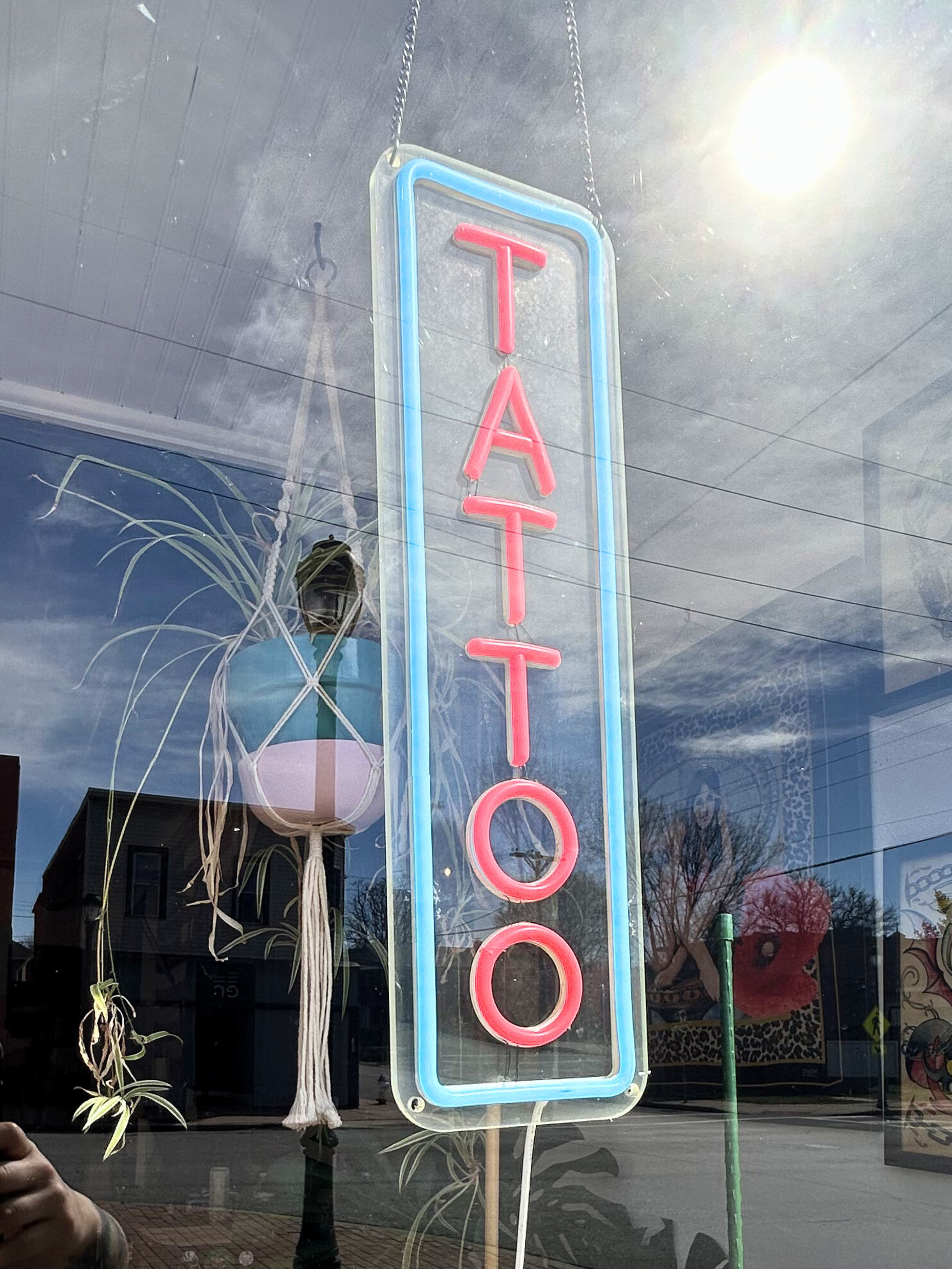 Neon sign reading 'TATTOO' in pink and blue colors displayed in a window with reflections of the street outside.