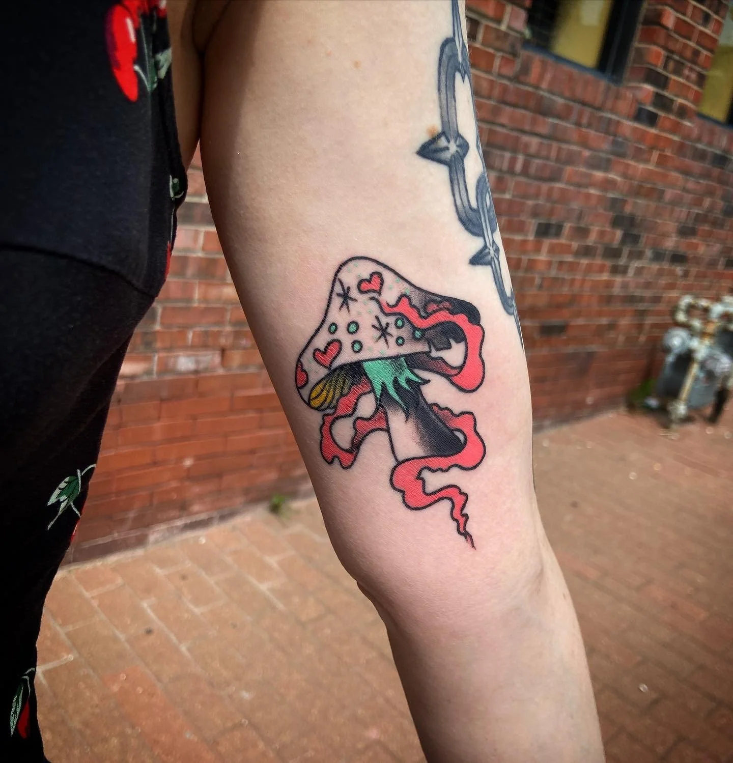 Colorful tattoo of a melting mushroom with a red vapor trail on person's forearm, with small hearts and other shapes on the mushroom cap.