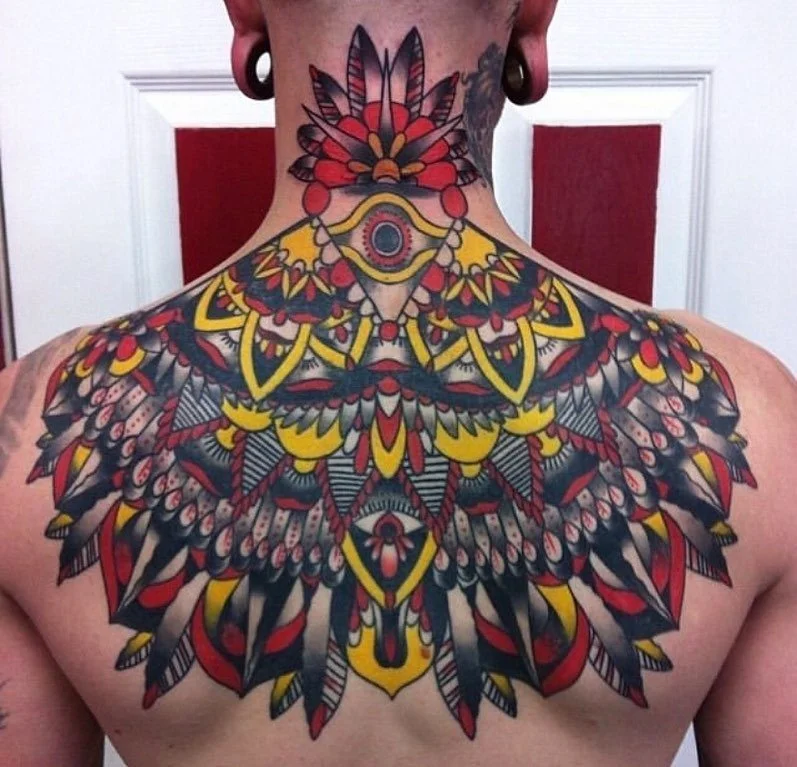 Colorful tattoo of an intricate symmetrical feather design covering the person's chest and neck.