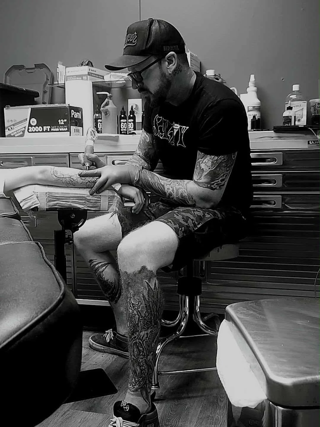 A tattoo artist working on a client's arm in a tattoo studio.