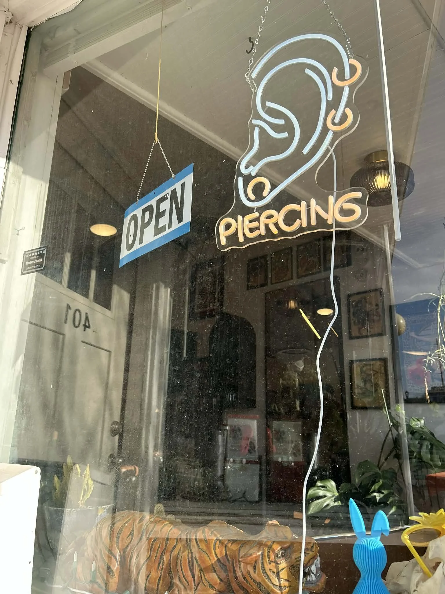 Neon sign for a piercing shop with an outline of an ear and the word 'PIERCING' below, and an 'OPEN' sign hanging on the window.