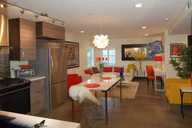 Open-concept living and dining area with colorful furniture, modern decor, and a kitchen in the background.