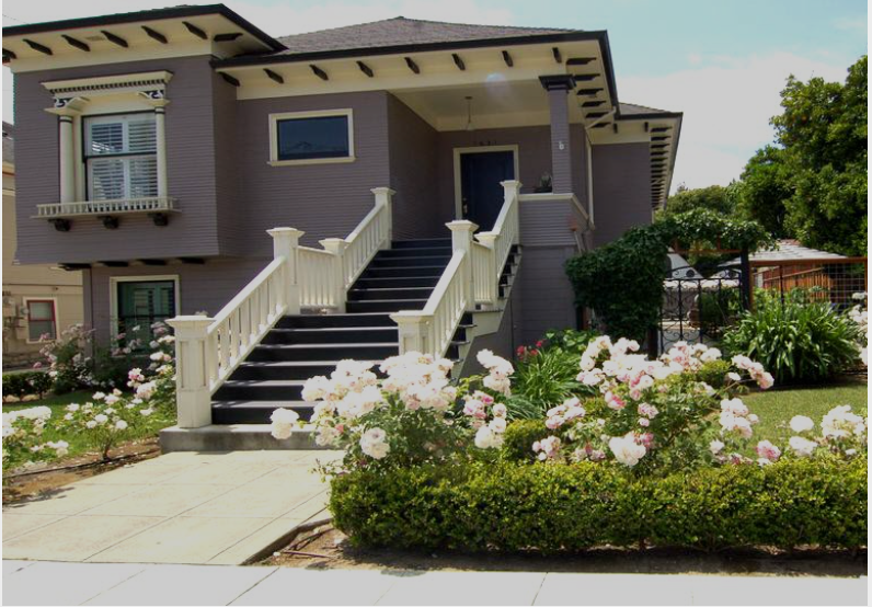 Front view of Napa's historic DeCurtin house (Wine Taster's Estate), with a staircase leading to a front porch, surrounded by a garden with pink and white flowers.