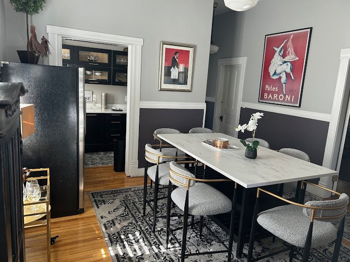 Dining area with a marble-top table, six upholstered chairs with metal frames, a floral centerpiece, and framed artwork on the walls.