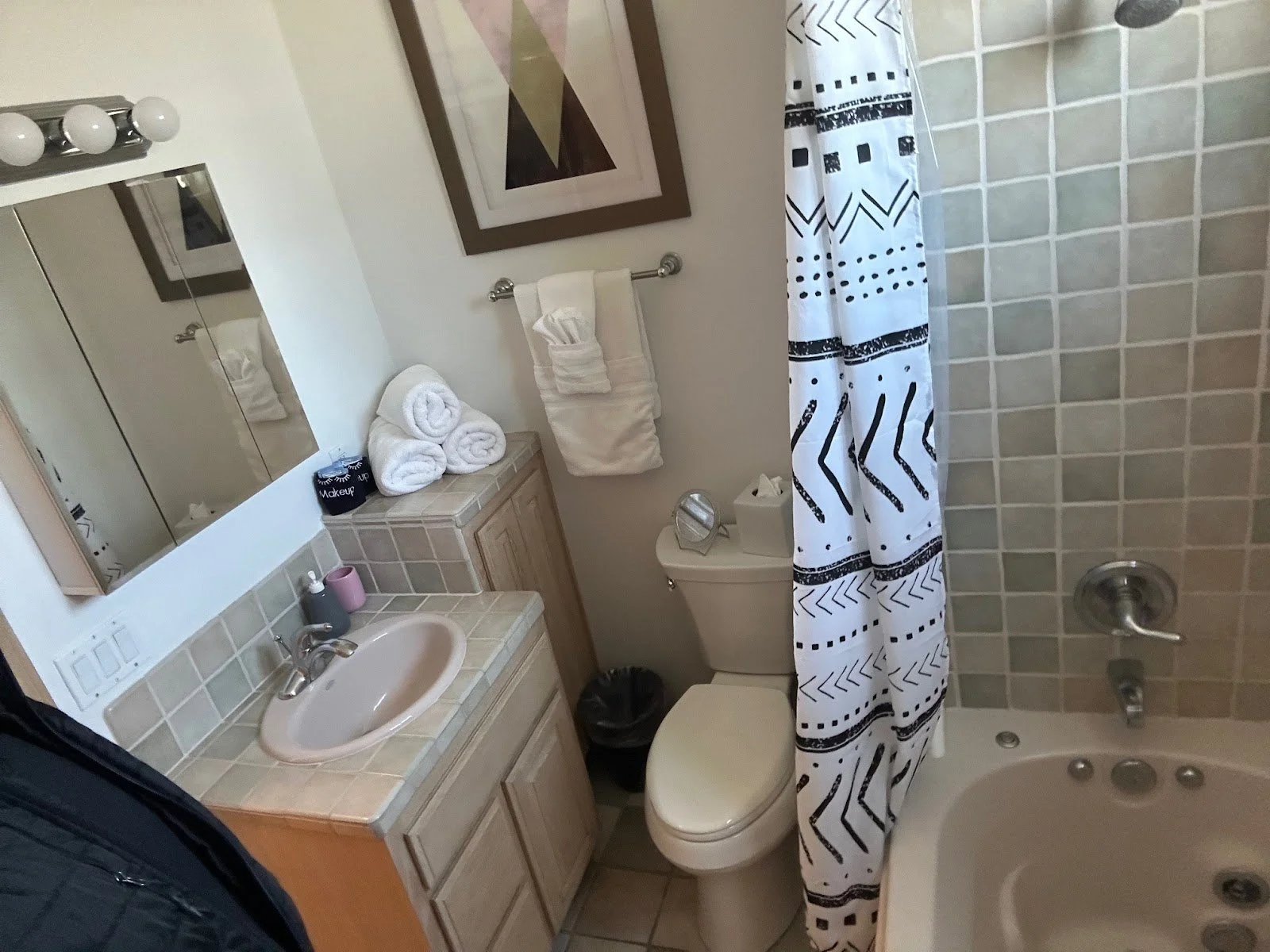 A bathroom with a vanity, mirror, towels, a toilet, and a bathtub with a patterned shower curtain.