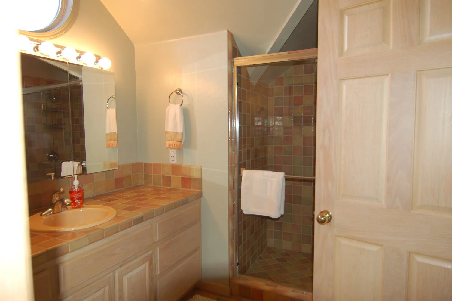 Bathroom with a sink, mirror, white towel, and shower area with tiled walls and floor.