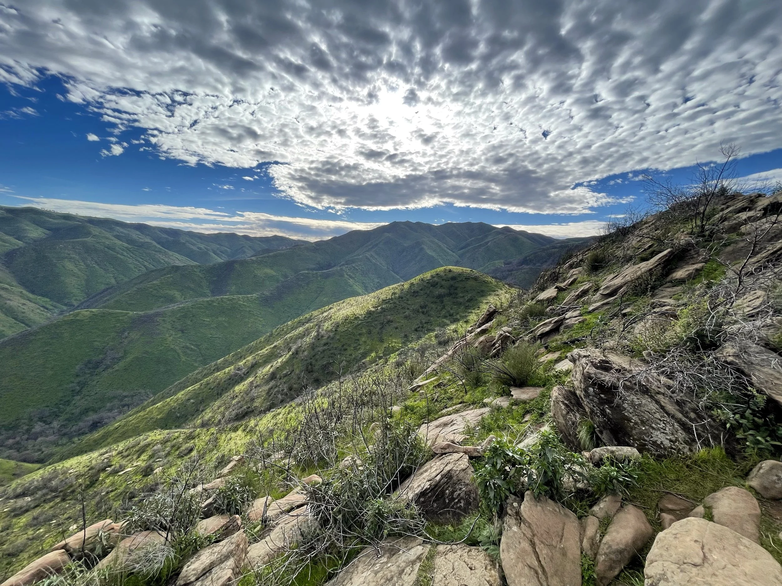 A scenic view of green rolling hills under a partly cloudy sky with sunlight peeking through.