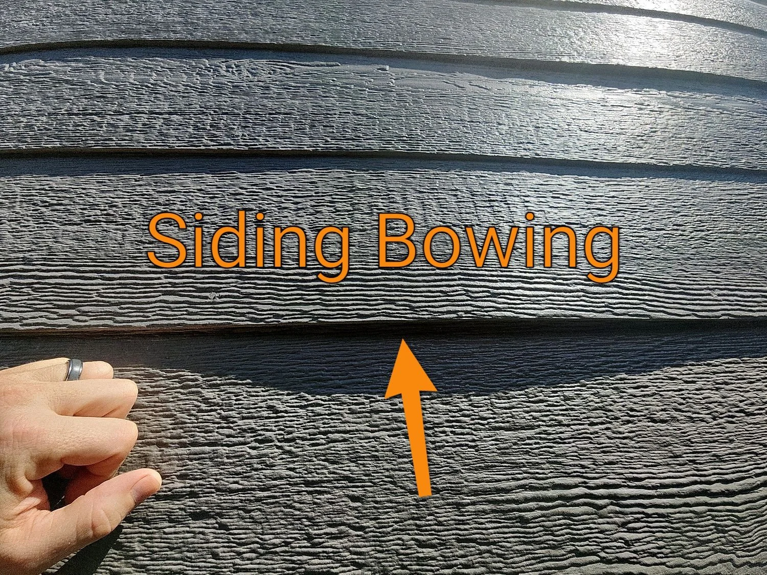 Exterior close-up showing fiber-cement siding bowing and creating a wavy wall surface, which may indicate improper fastening, uneven framing, or moisture issues behind the siding.