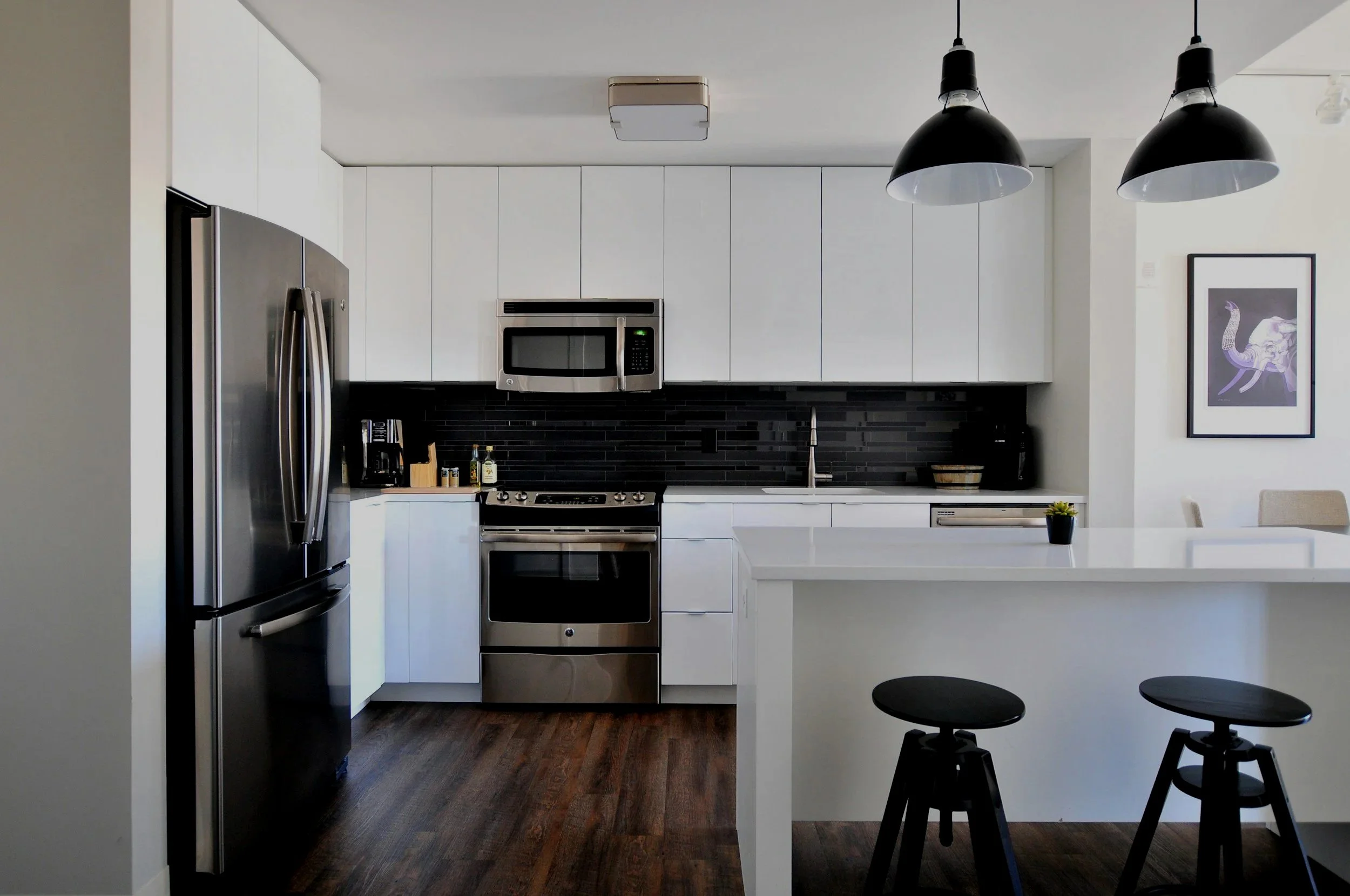 Hero image of a modern grey kitchen with a subtle grey overlay, featuring cabinets, island, and stainless steel appliances, used as a website banner background.