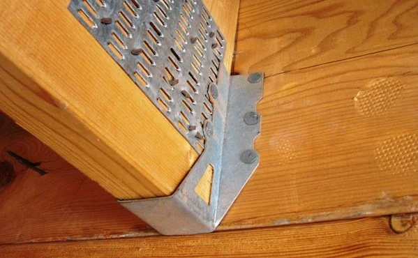 Close-up of a galvanized steel joist hanger securing a wood joist to a supporting beam, showing the structural connection hardware used in deck and framing construction.