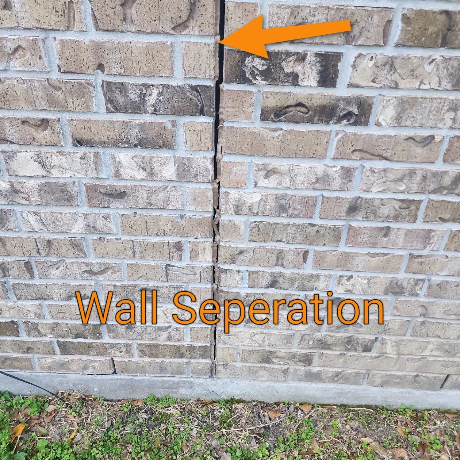 Close-up of brick veneer at the roofline showing separation along a vertical mortar seam where the veneer meets the roof flashing.