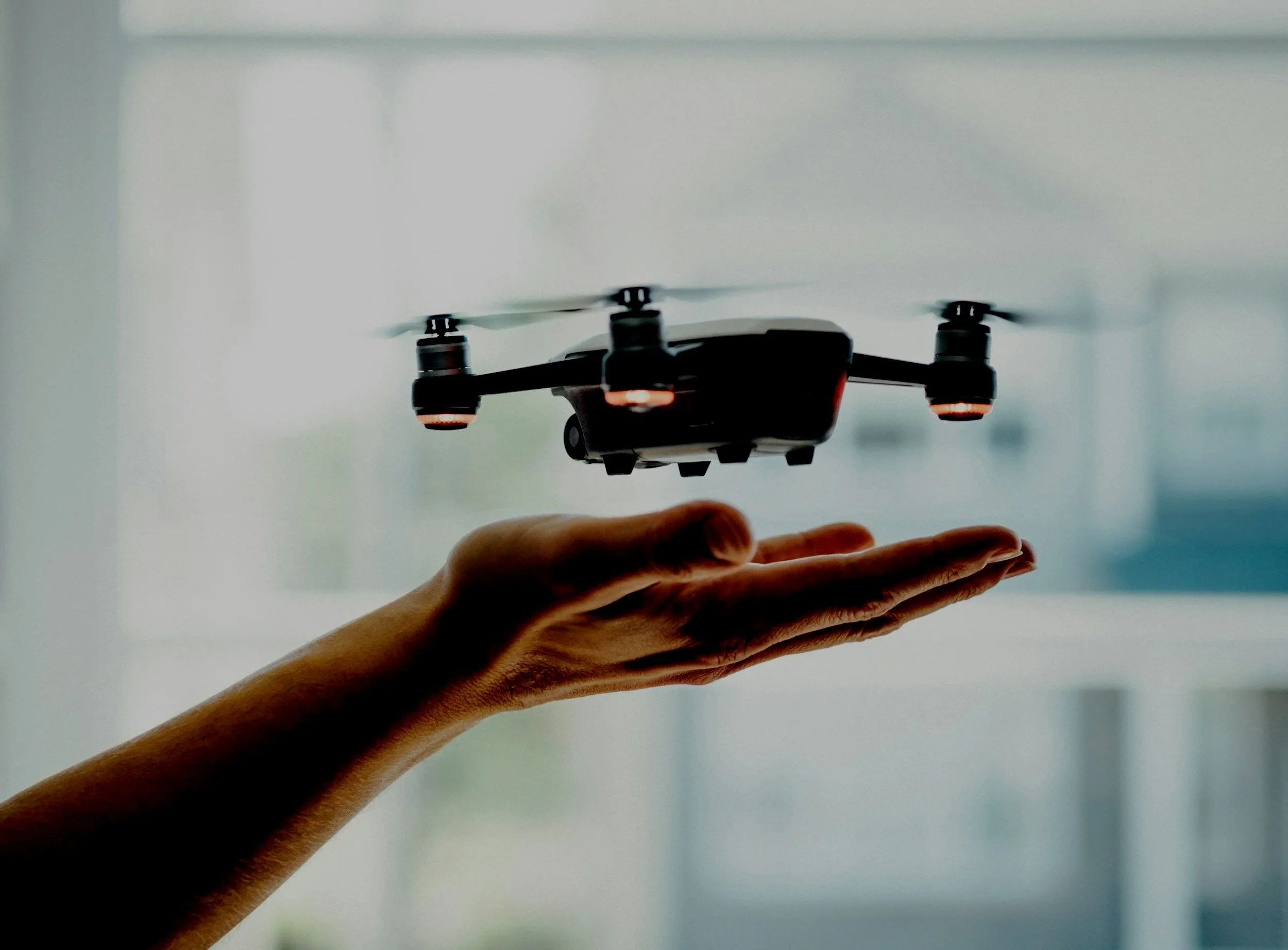 Close-up of a small quadcopter drone hovering a few inches above an outstretched hand, demonstrating precise flight control.