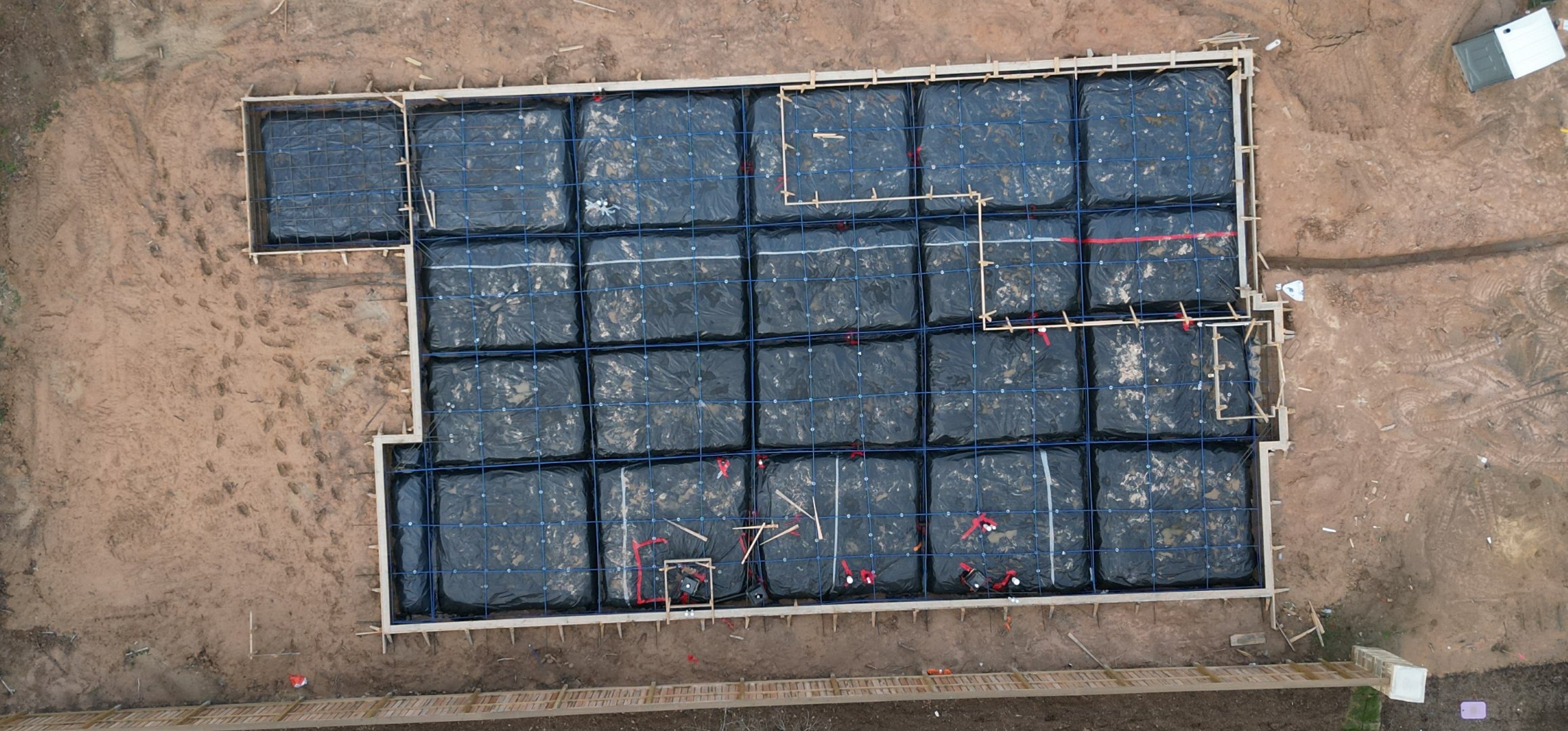 Aerial hero image of a Phase 1 pre-pour foundation inspection with a subtle grey overlay, showing the full post-tension slab layout, forms, and reinforcement for a new home.