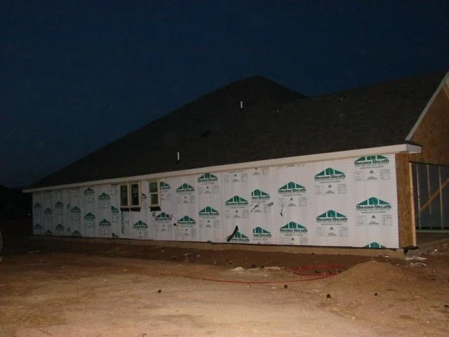 New construction home covered in Tyvek housewrap at night during a phase 2 pre-drywall inspection.