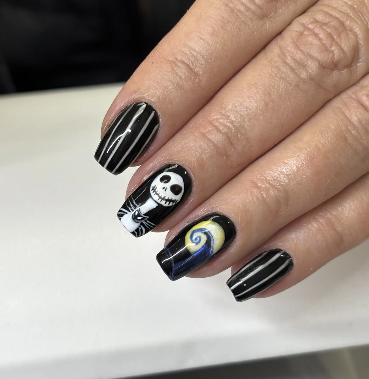 Nail art featuring black and white striped design, a Jack Skellington face, and a swirl resembling Vincent van Gogh's Starry Night.