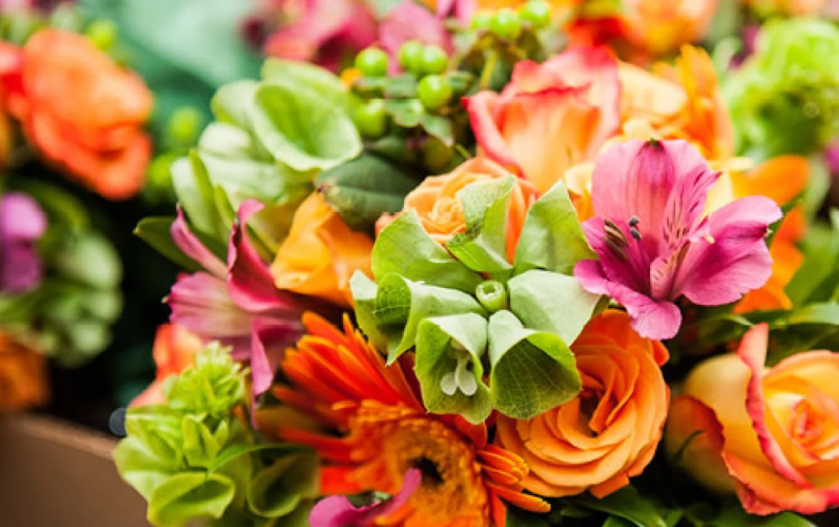 Close-up of a colorful bouquet of flowers including roses, lilies, and other blooms in shades of orange, pink, and green.
