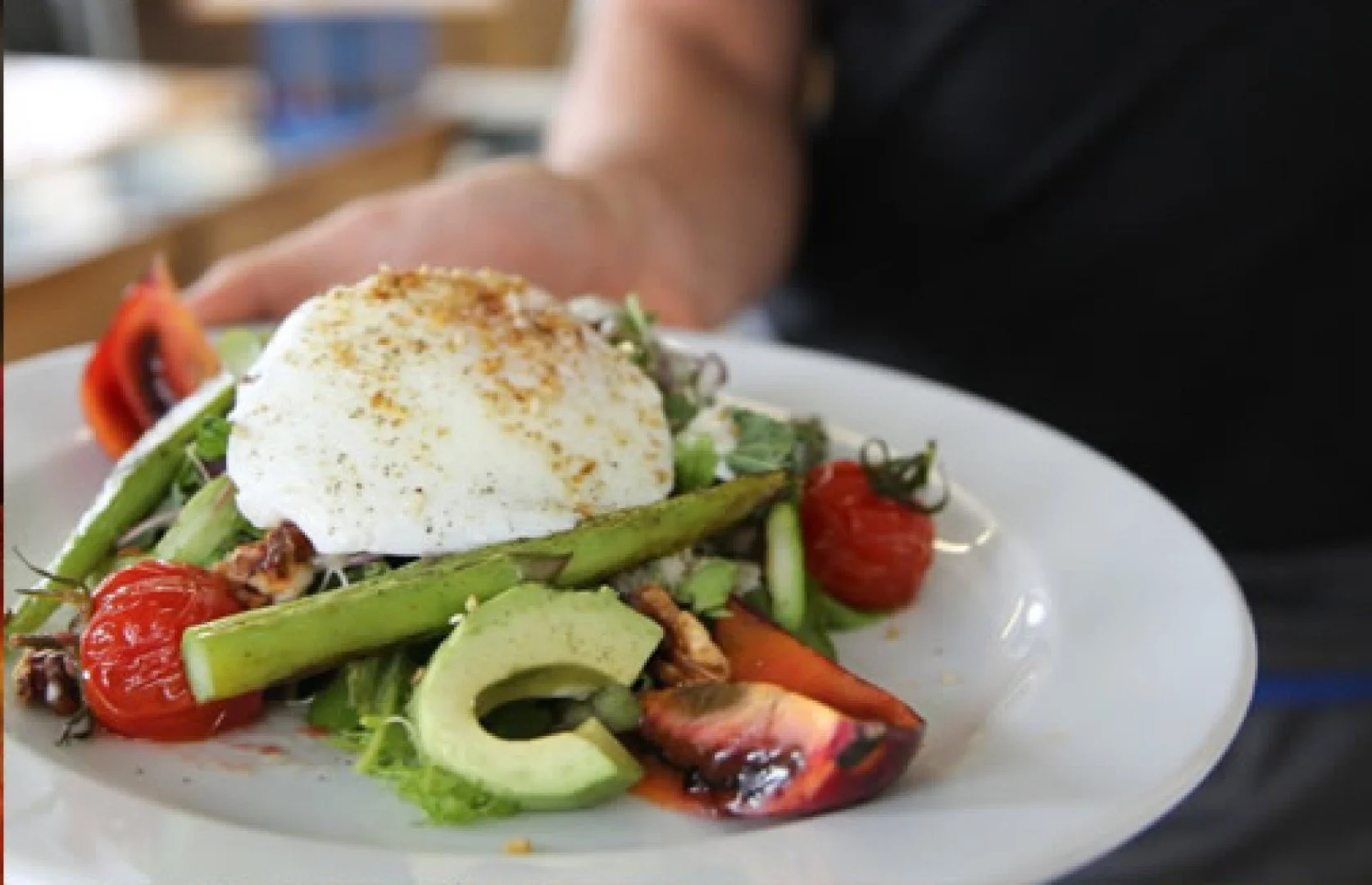 Salad with cherry tomatoes, avocado, asparagus, mixed greens, topped with a poached egg and sprinkled with spices.