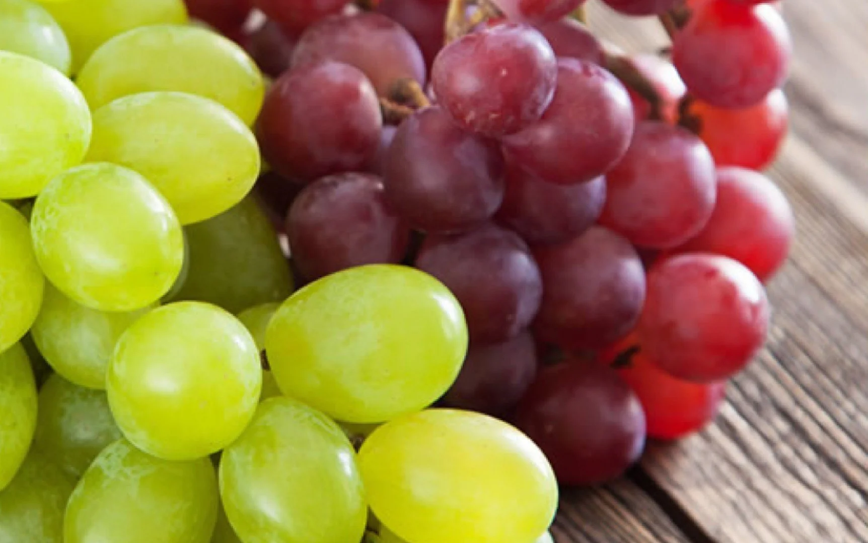 Close-up of green and red grapes on a wooden surface.