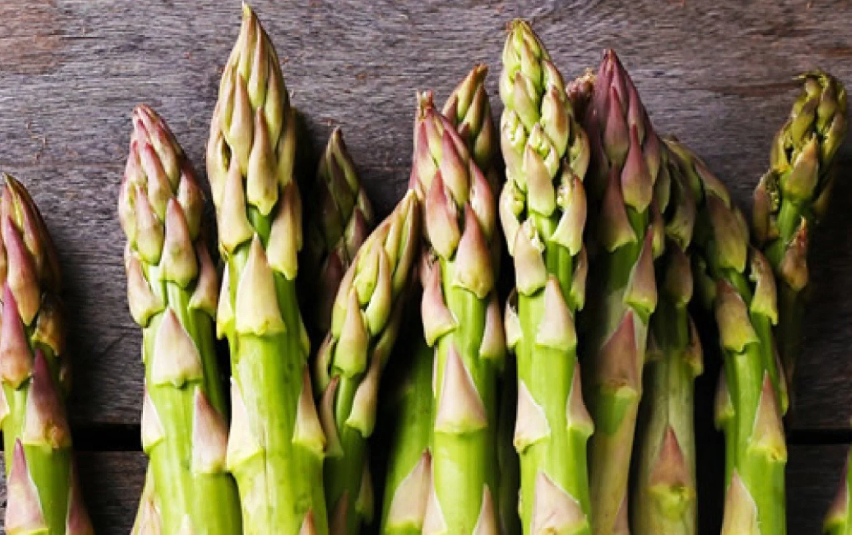 Multiple fresh asparagus spears arranged on a wooden surface.