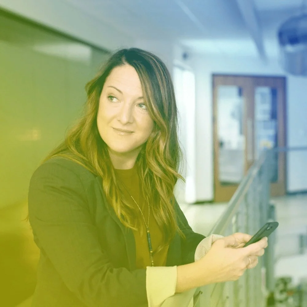 Kvinne lener seg over et gelender med en mobil i hendene