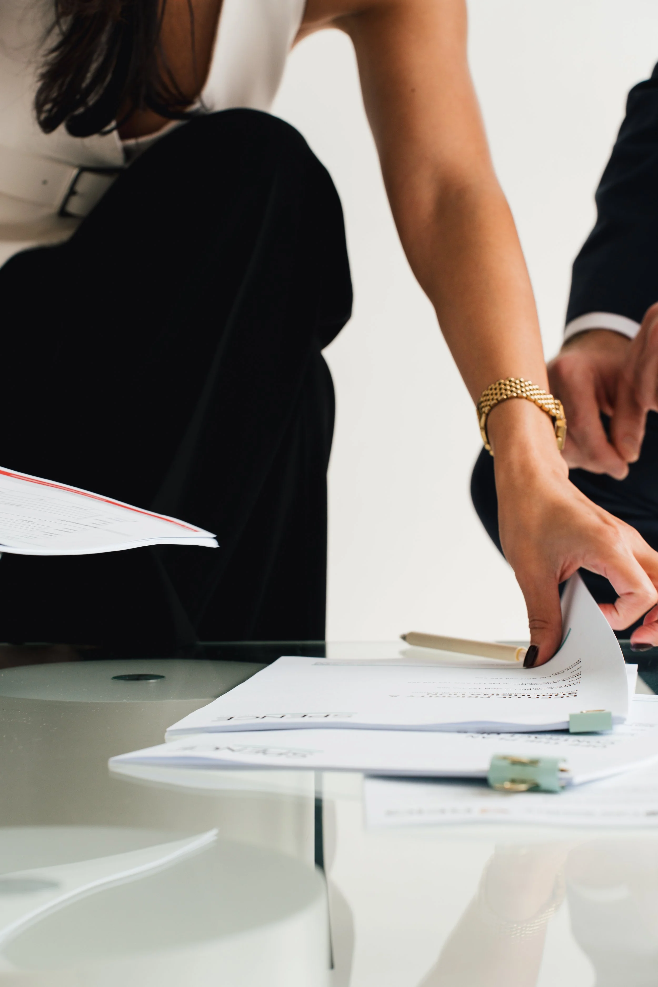 People in business attire organize documents and papers on a glass table, with a white background.