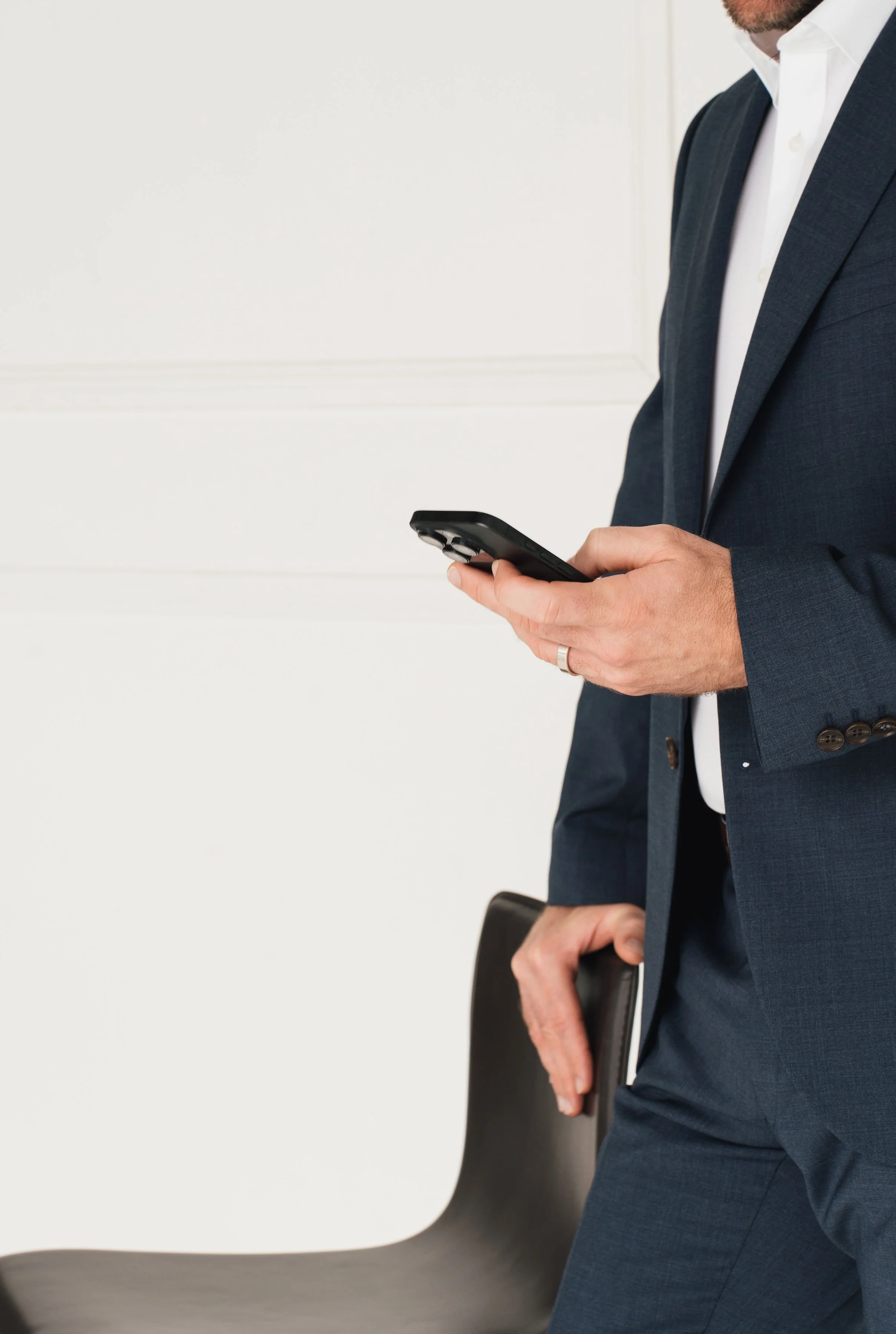 Man in a navy suit holding a smartphone and a black notebook in a modern office setting.