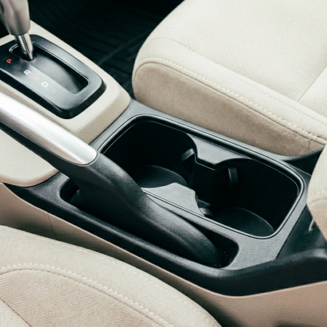Interior of a car showing the gear shift, cup holder, and beige seats.