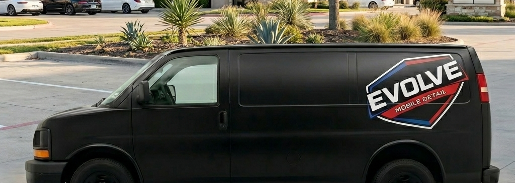 A black cargo van with a large 'Evolve Mobile Detail' logo on its side, parked in a parking lot with some plants and trees in the background.