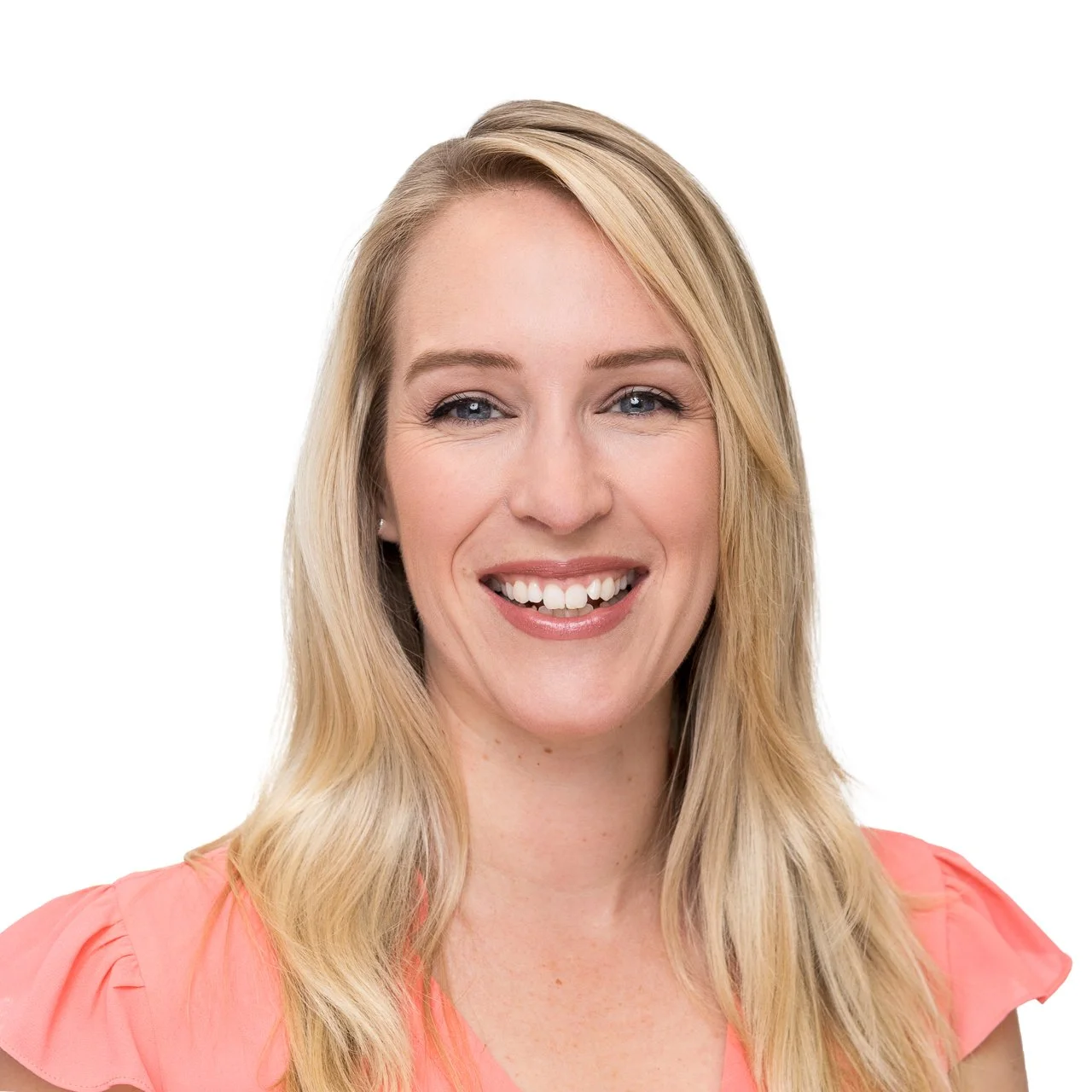 Close-up of a smiling woman with blonde hair, blue eyes, wearing a coral pink top, against a plain white background.