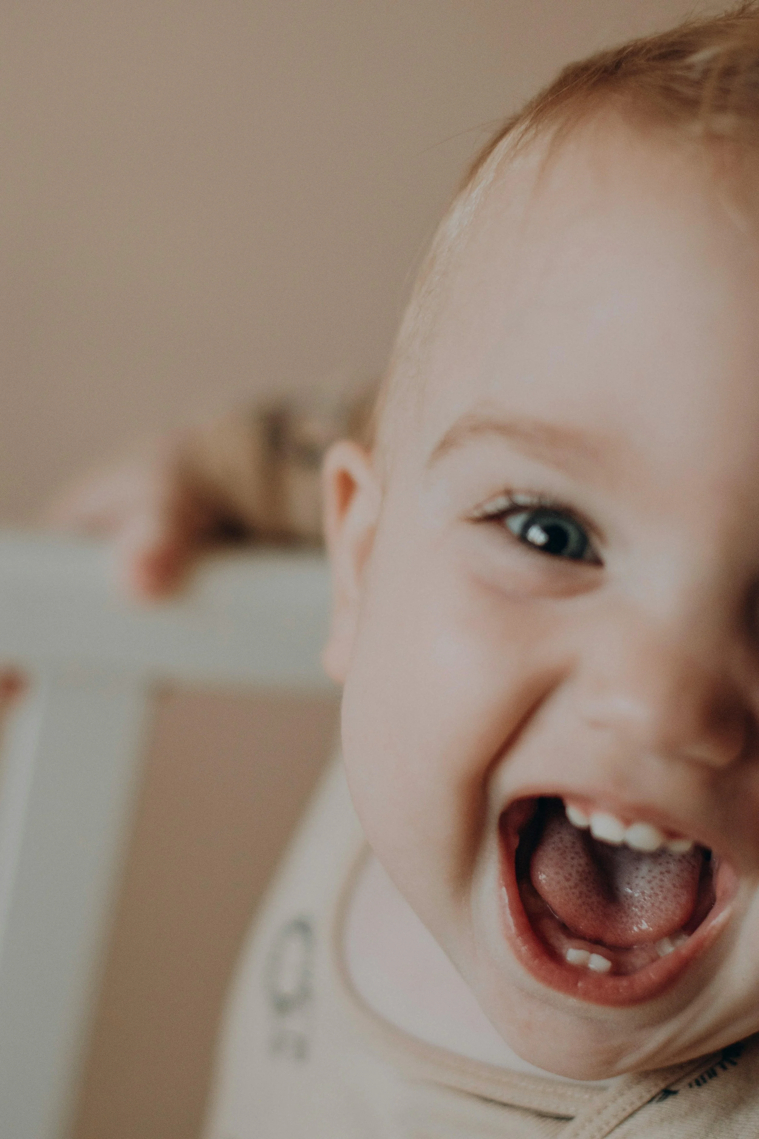Close-up of a young child's face with red hair, blue eyes, and an open-mouthed smile showing teeth, expressing joy or excitement.