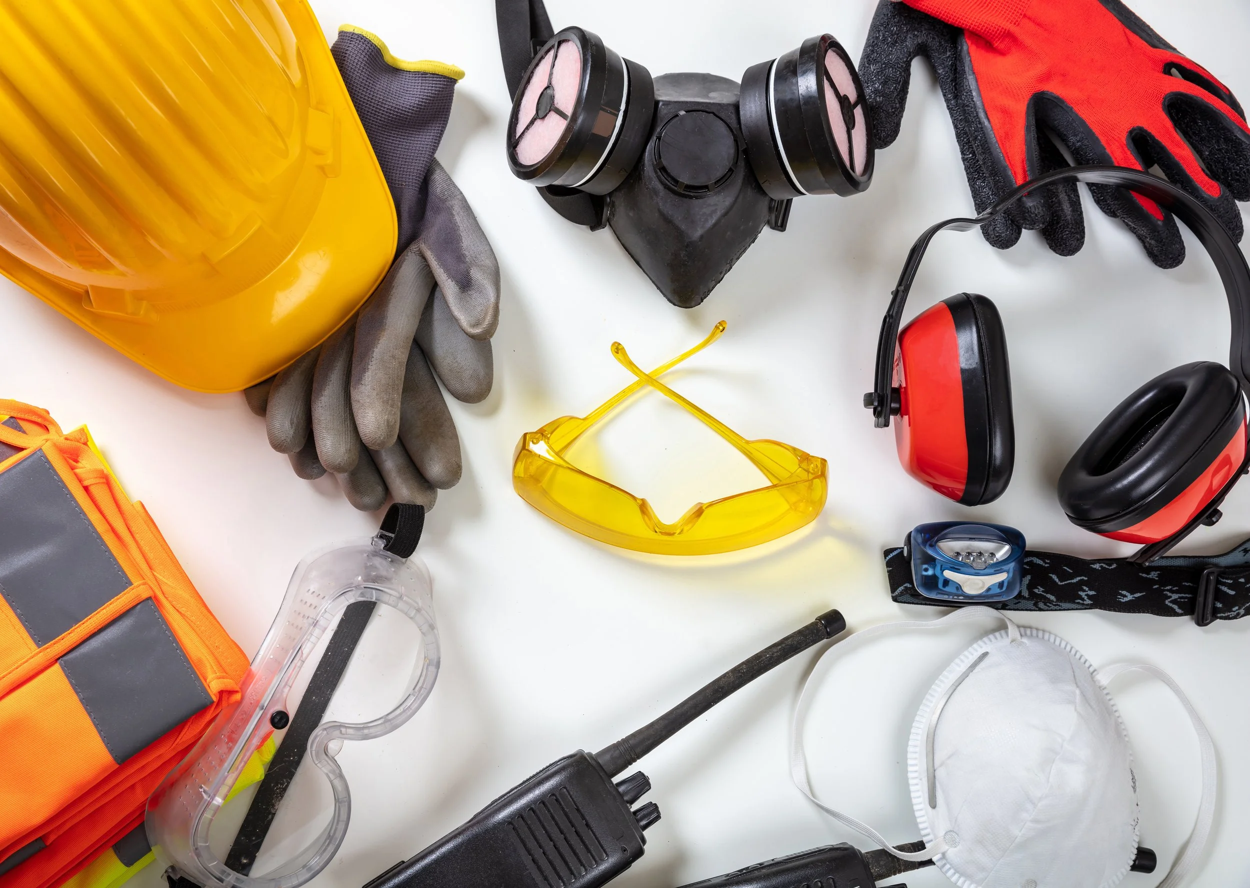 Personal protective equipment and safety gear including yellow hard hat, gloves, gas mask, ear protection, safety goggles, vest, mask, multimeter, and a walkie-talkie.
