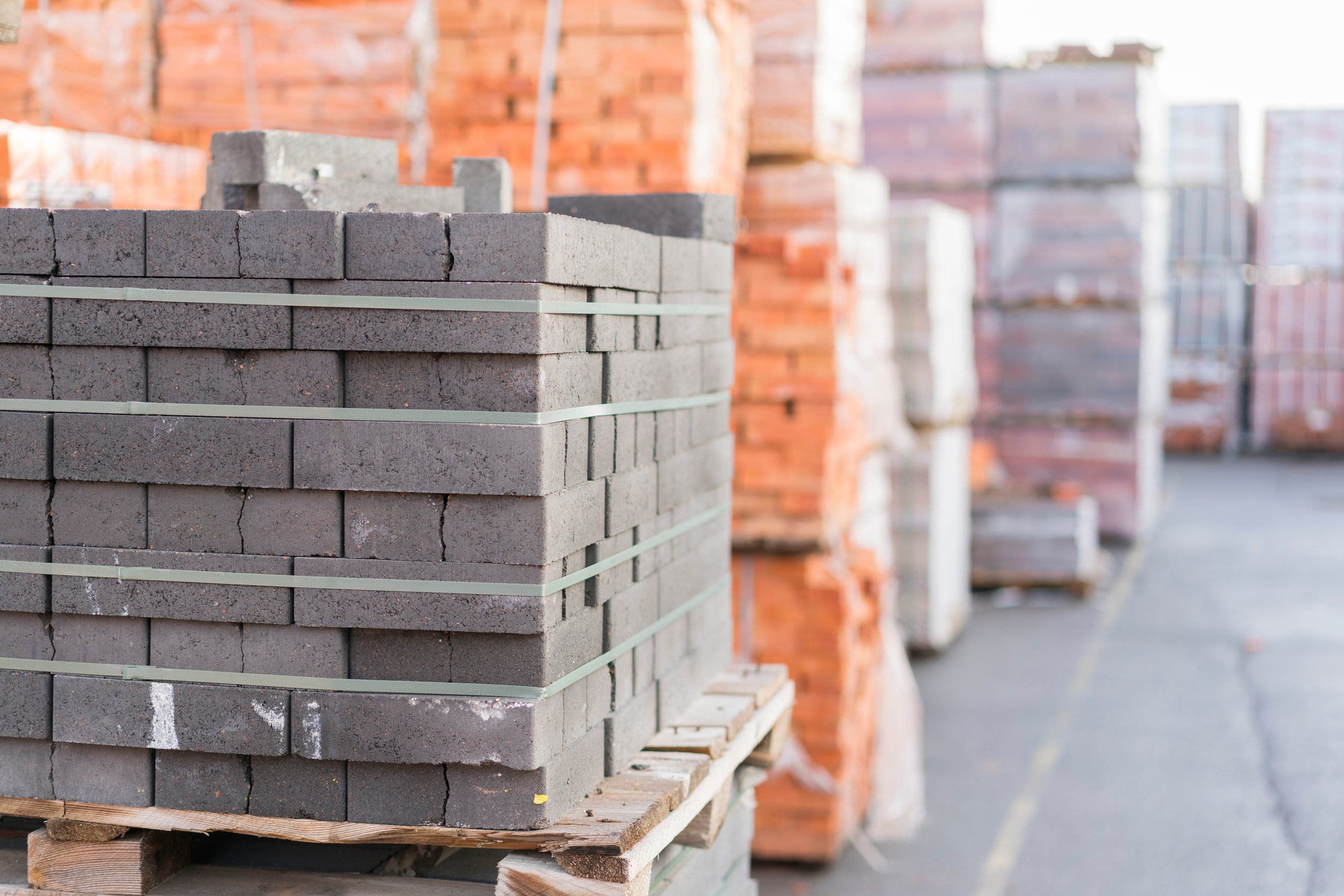 Pallets of gray, reddish, and grayish-brown bricks stacked outdoors on a construction site.