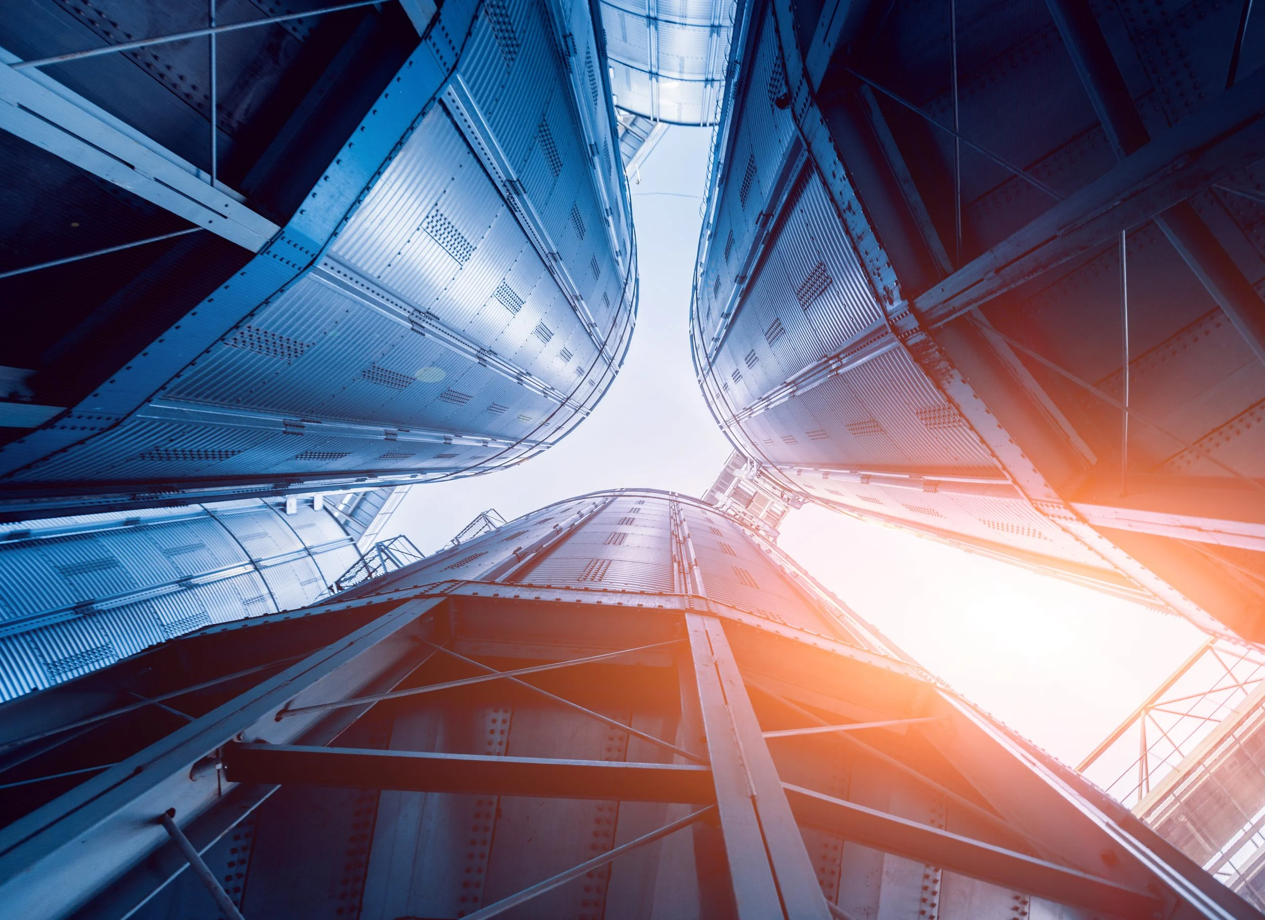 Looking up at the sky through the narrow space between four tall modern buildings made of metal and glass.