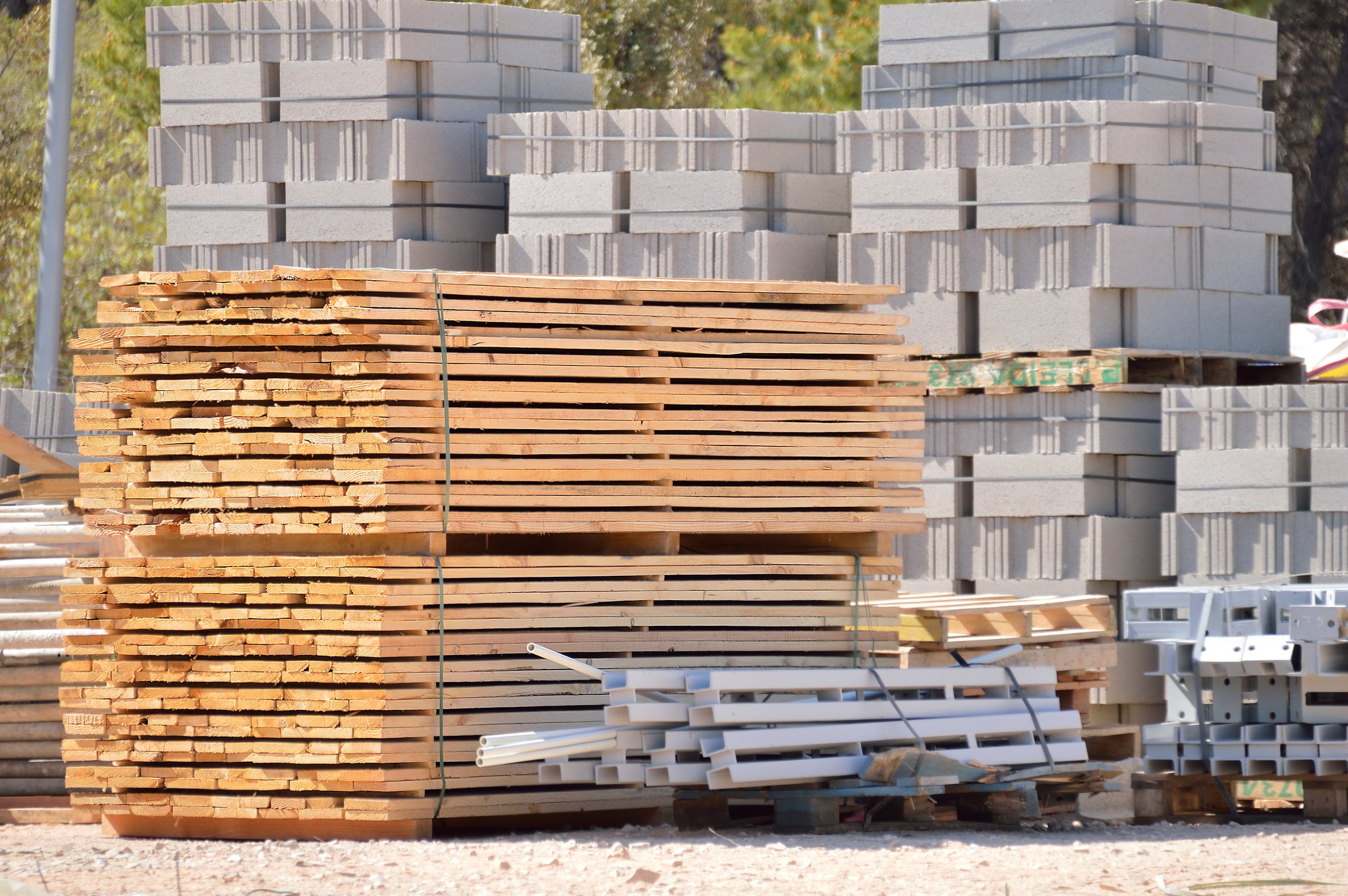 Construction site with stacks of wooden planks, concrete blocks, metal beams, and other building materials.
