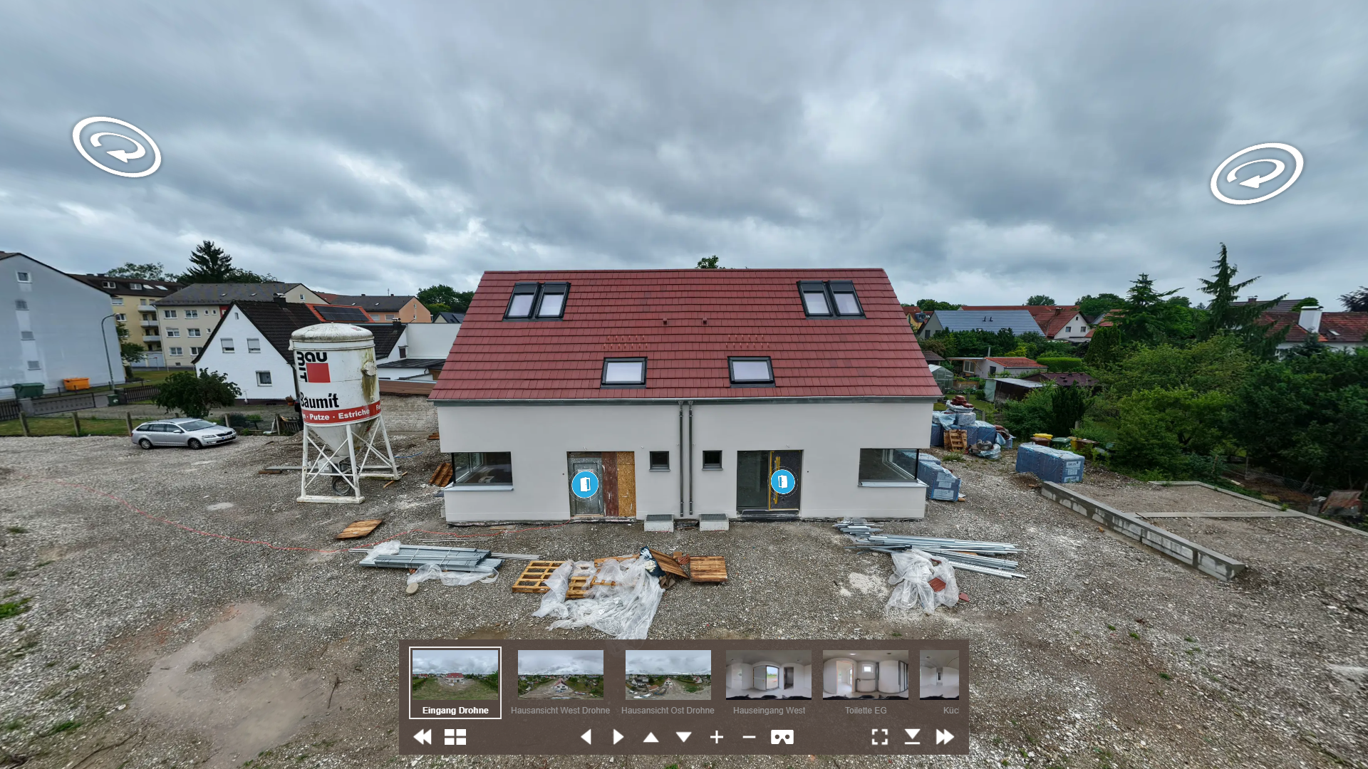 Ein mehrstöckiges Haus unter Bau mit roten Dachziegeln, Bauarbeiten im Gange, umgeben von Baum- und Wohnhäusern, bei wolkigem Himmel.
