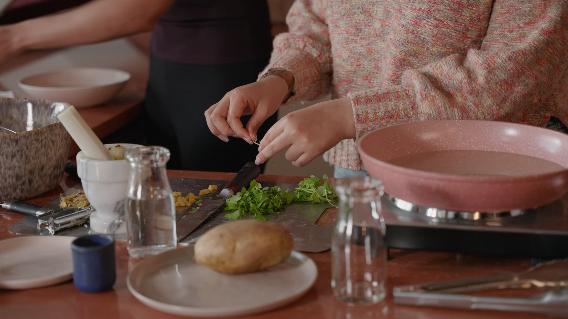 Person preparing food by chopping cilantro on a cutting board in a kitchen