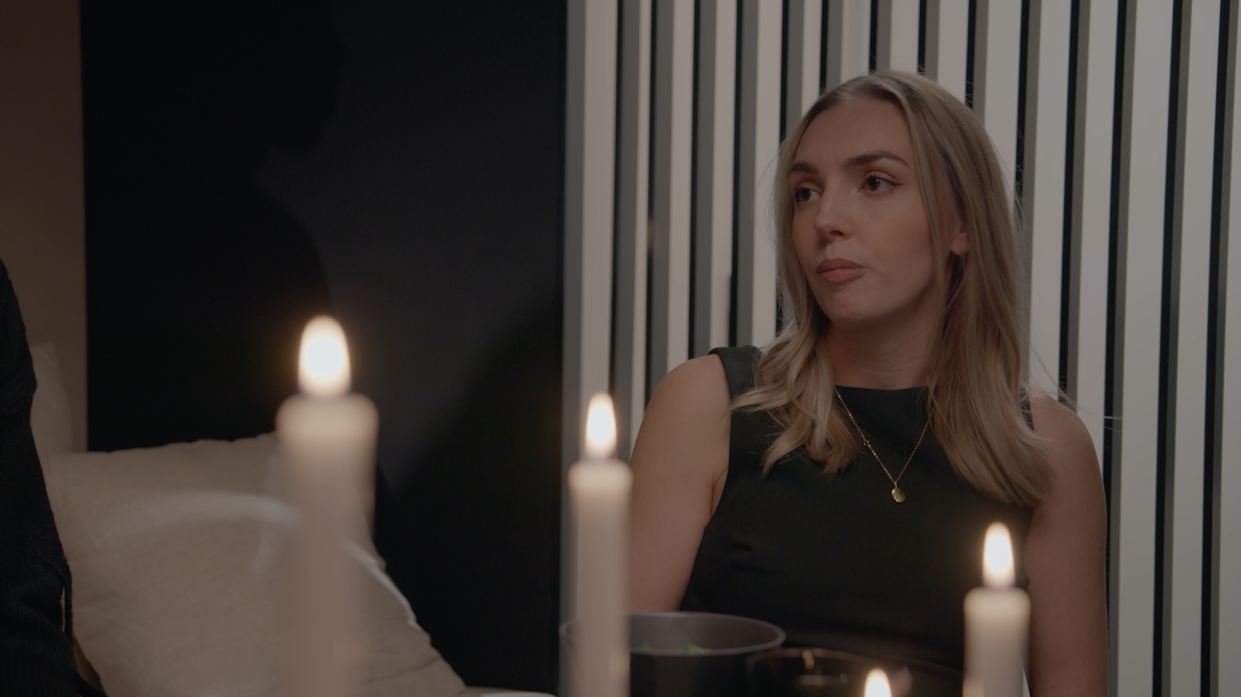 Blonde woman in a black sleeveless top seated at a candlelit dinner table