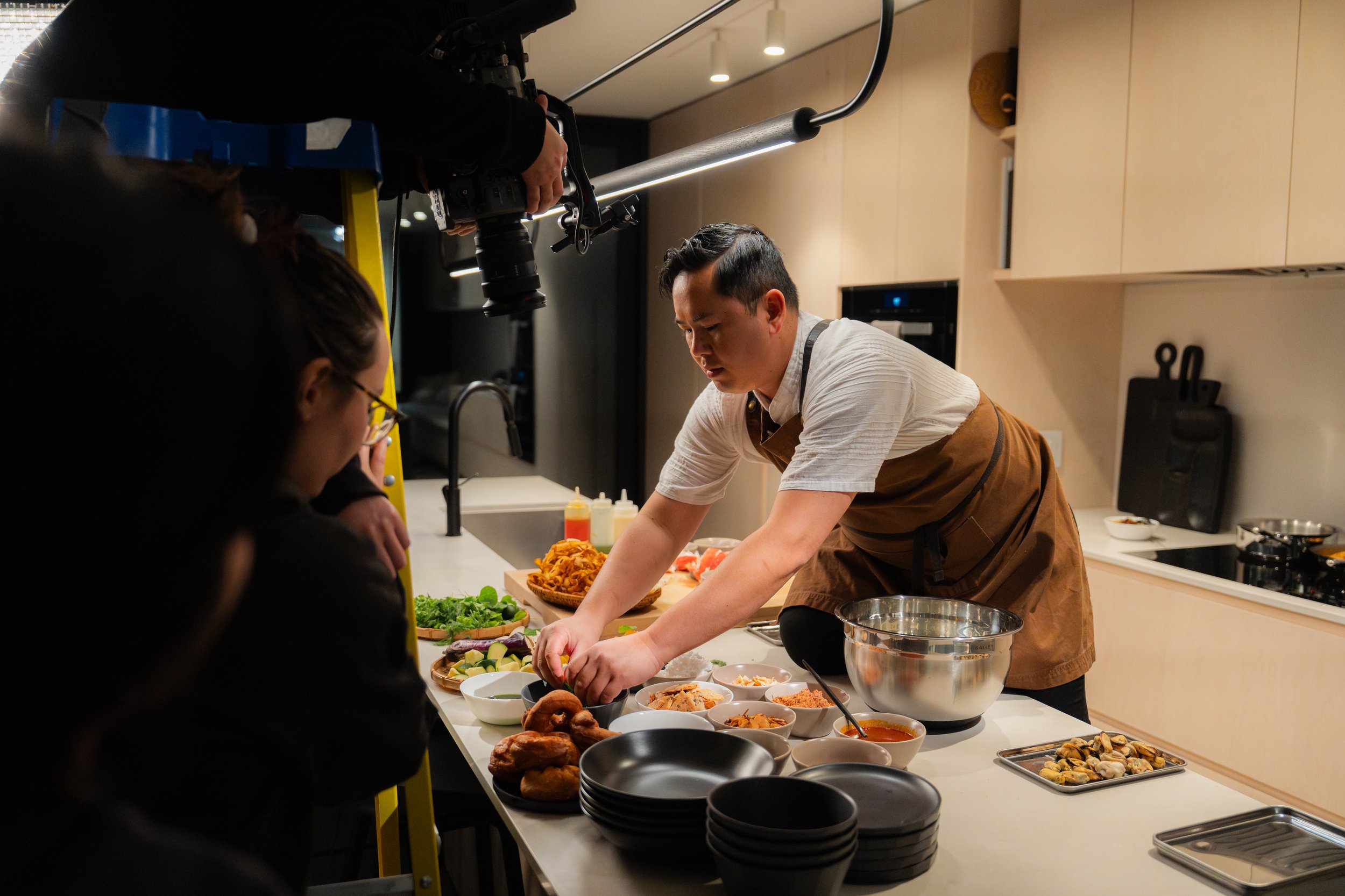 Chef preparing food in a modern kitchen while being filmed by a camera operator