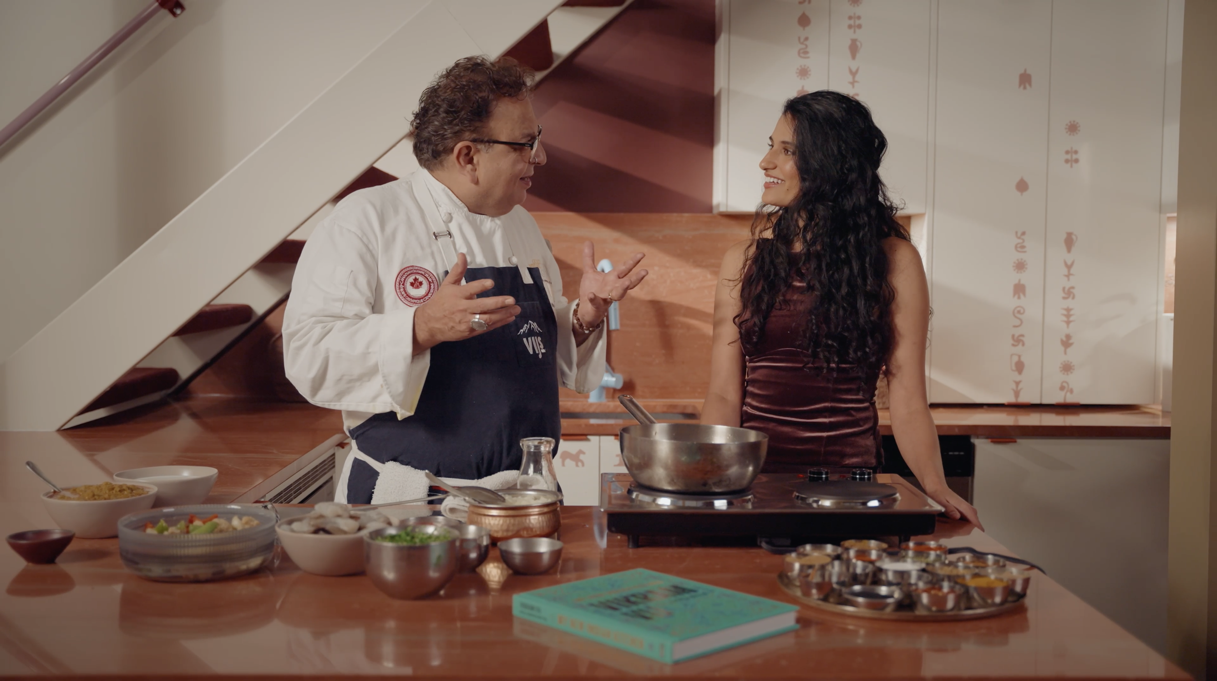 Chef and woman preparing food together in a modern kitchen with ingredients and spices on the counter