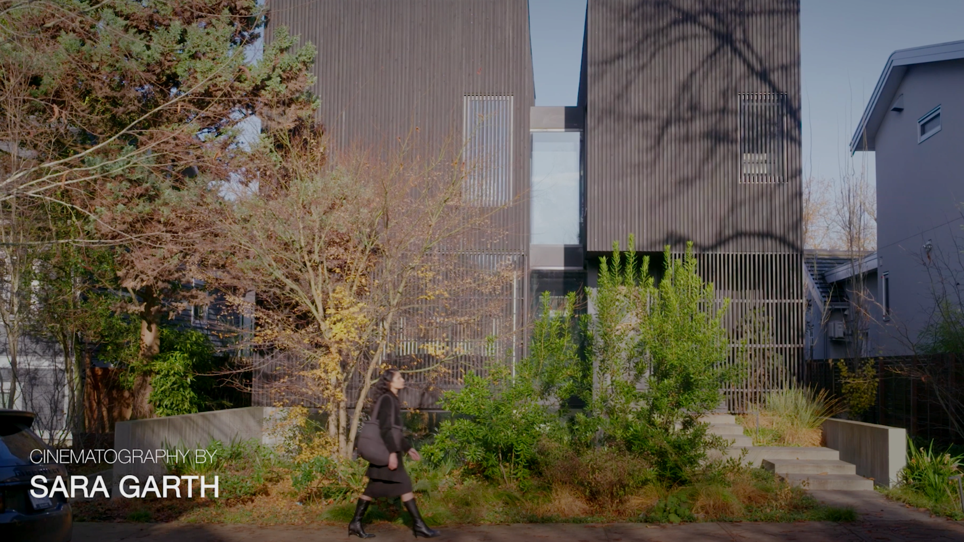 Modern slatted-wood house with landscaped garden and woman walking in front