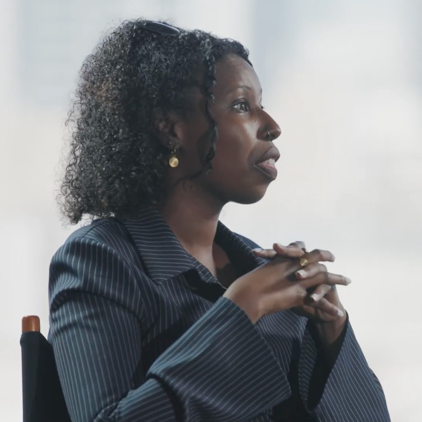 Black woman in a pinstripe blazer speaking in profile with her hands clasped